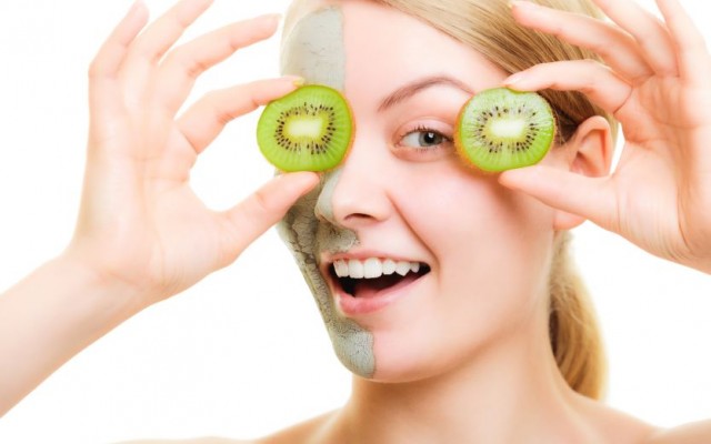 Skin care. Woman in clay mud mask on face holding slices of kiwi fruit isolated. Girl taking care of dry complexion.